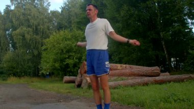 Bu enerjik videoda, beyaz tişörtlü ve mavi şortlu bir adam atlama yeteneğini parkta gösteriyor, toprak yolda güvenle zıplıyor.