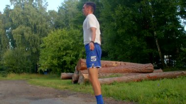 Beyaz gömlekli ve mavi şortlu bir adam parkı keşfediyor, doğanın tadını çıkarıyor. Toprak bir yolda koşuyor, aktif yaşam tarzını vurguluyor.