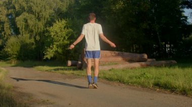 Bir adam, dingin bir ormanlık alanda, manzaralı bir toprak yolda ip atlayıp etkinliğini ve doğanın güzelliğini vurgulayarak zindeliğini sergiliyor.