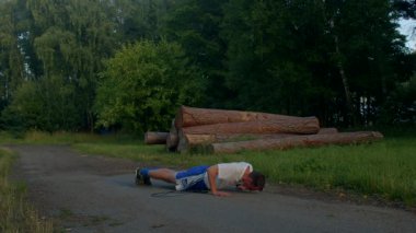 Formda bir adam şınav çekerek güç ve dayanıklılık gösterir. Zeminde kütüklerle başlıyor, sonra da spor yapmaya kararlı olduğunu vurgulayan sessiz bir yolda.