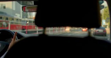 Bir adam arabasını hareketli bir şehirde sürüyor, kalabalık caddelerde geziniyor ve şehir hayatının dinamik atmosferini modern mimariyle yakalıyor.