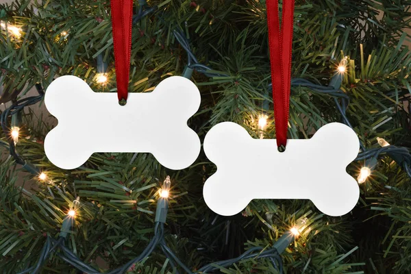 Closeup of two dog bone shaped Christmas Ornaments hanging merrily from a lit up Christmas tree.