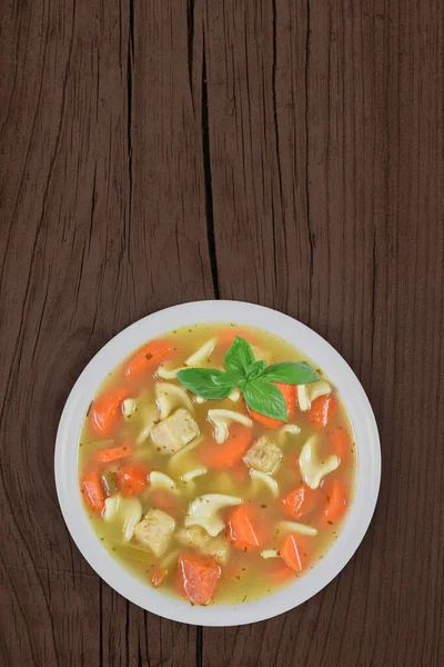 Top view of home cooked chicken noodle soup with fresh carrots and extra chicken. Set atop a warm rustic wood background with plenty of copy space.