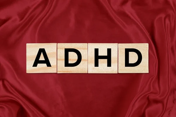 Closeup of wooden tiles spelling out ADHD against a restless red silk background.