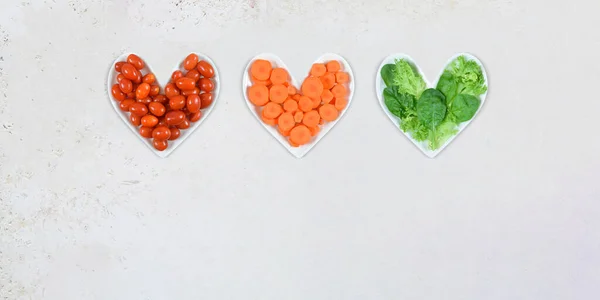 Photo of tomatoes, carrots and lettuce on heart shaped plates atop a white stone background. Plenty of copy space.