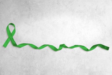 Açık gri beton arka planda kıvrık uçlu yeşil bir kurdelenin fotoğrafı. Kopyalama alanı çok.