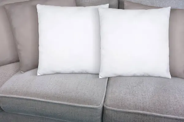 Two square white throw pillows lazily enjoying naptime on a tan modern sofa.