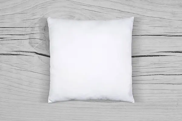White throw pillow resting in style atop a light gray weathered wooden surface.