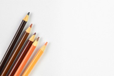 Bir avuç dolusu kahverengi ve bej renkli kalem beyaz bir arkaplanda sanatsal olarak düzenlenmiş ve kopyası için bolca yer var.