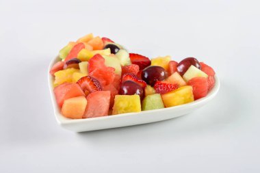 Renkli meyve salatası ve kalp şeklinde bir tabak yakın plan. Arkaplan, pankart ve editoryal kullanım için ideal.