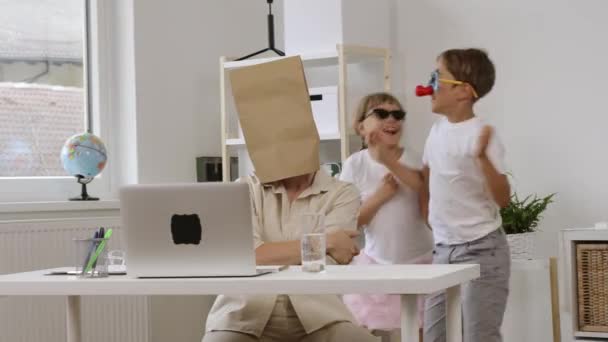 若いです母で覆われた頭で紙袋でラップトップ子供たちは背景で遊んでいます — ストック動画