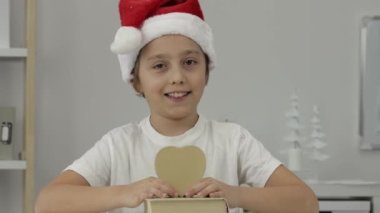9 yıllık Noel Baba şapkalı çocuk kalp şeklinde bir kutu tutuyor. - Yakın çekim. Yüksek kalite 4k görüntü