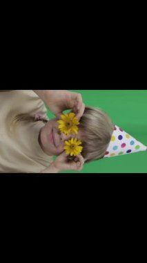 Face of funny girl of 7 years with cone hat and yellow daisies. Green screen background. Closeup. High quality footage