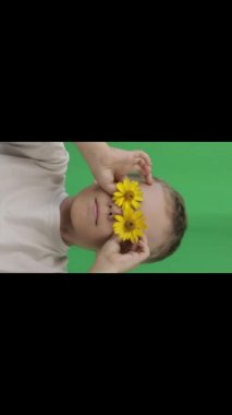 Boy of 9 years covered his eyes with yellow daisies. Closeup. High quality footage
