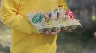 Girl of 7 years dressed in yellow pullover keeps decorated Easter eggs in the palms. High quality 4k footage