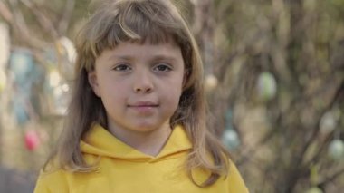 Girl of 7 years dressed in yellow pullover keeps decorated Easter eggs in the palms. High quality 4k footage