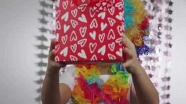 Boy of 10 years old dressed in clowns wig and eyeglasses. He keeps a bag with a present . High quality 4k footage
