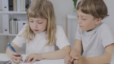 Boy of 9 years old helps his younger sister to make her homework. High quality 4k footage