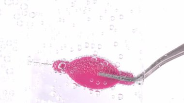 Interdental brush in a metallic pincette in a sparkling water. Closeup