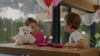 Boy and girl are sitting at the bar table in the decorated room for Valentines Day. Medium shot 