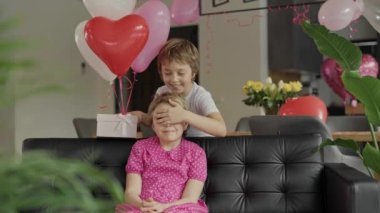 Boy closes the eyes to the girl sitting in the sofa. High quality 4k footage