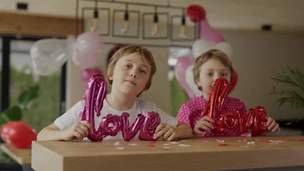 男の子と女の子はバレンタインデーの装飾された部屋のバーテーブルに座っています — ストック動画