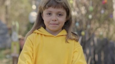 Girl of 7 years dressed in yellow pullover keeps decorated Easter eggs in the palms. High quality 4k footage