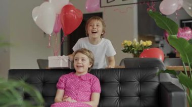 Boy and girl are laughing at the sofa in the decorated room for Valentines Day. High quality 4k footage