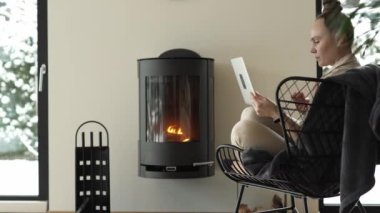 Female sits in the armchair close to the real chimney and works at laptop. High quality 4k footage