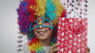 Boy of 10 years old dressed in clowns wig and eyeglasses. He keeps a bag with a present . High quality 4k footage