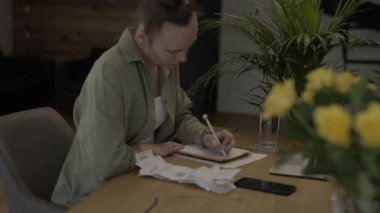 Female is making some calculations. Bills and pc are in the background