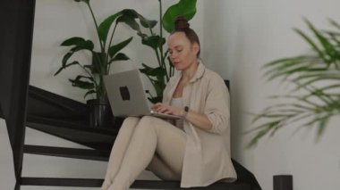 Female works at laptop sitting on the steel stairs. High quality 4k footage