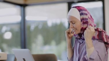 Female in hijab is sitting at the table in front of a laptop. High quality 4k footage
