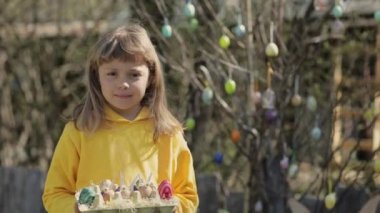 Girl of 7 years dressed in yellow pullover keeps decorated Easter eggs in the palms. High quality 4k footage