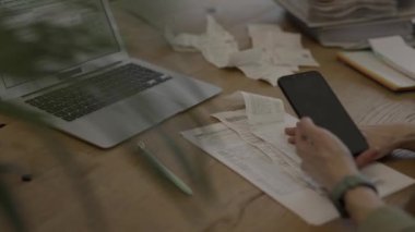 Female scans a bar code with her phone. Bills, tax form, and pc are in the background