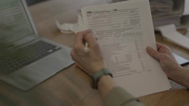 Female fills up the tax form at the table. Bills and pc are in the background