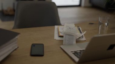 Bills, copy book, pc, folders, phone on the table.Female is sitting at the table. 