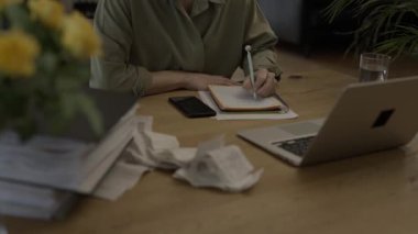 Female fills up the tax form at the table. Bills and pc are in the background