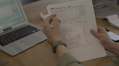 Female fills up the tax form at the table. Bills and pc are in the background