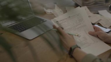 Female fills up the tax form at the table. Bills and pc are in the background