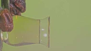Bir bardak Türk çayı ve yeşil ekranda gümüş bir tabakta hurma. Dikey çekim