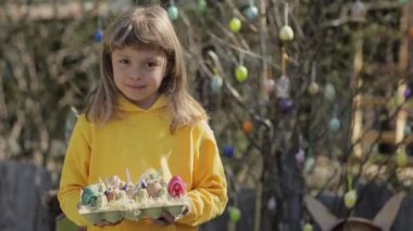 Girl of 7 years dressed in yellow pullover keeps decorated Easter eggs in the palms. High quality 4k footage