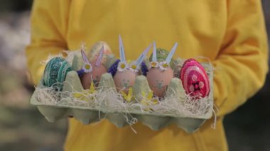 Girl of 7 years dressed in yellow pullover keeps decorated Easter eggs in the palms. High quality 4k footage
