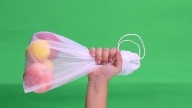 Childs hand is holding a sustainable bag with fruits at a green screen. High quality footage