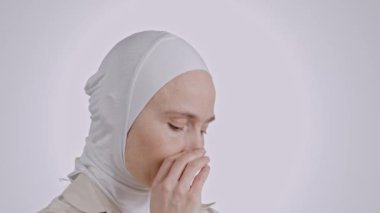 35-40 yaşları arasında başörtüsü takmış genç Müslüman bir kadın ağzını palmiye ile kapatıyor.