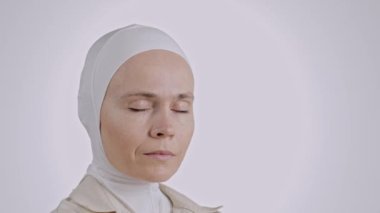 35-40 yaşları arasında ciddi bir Müslüman kadın. Başörtüsü takmış. Kameranın önünde gözlerini açıyor.