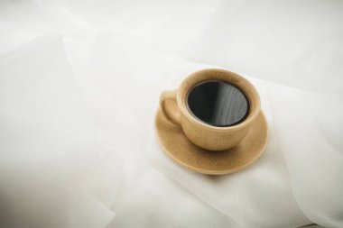 Pencerenin kenarında beyaz perdeli bir fincan kahve duruyor.