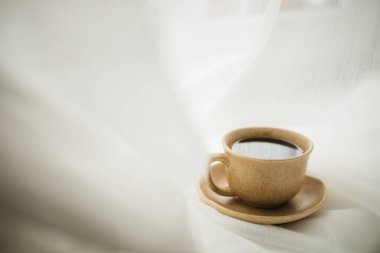 Pencerenin kenarında beyaz perdeli bir fincan kahve duruyor.