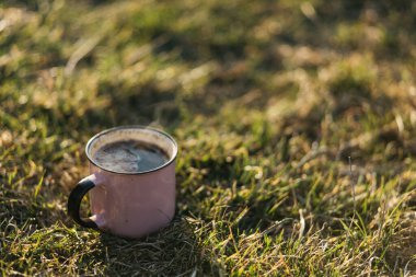 Gün batımında yeşil çimlerde kahve standı olan metal bir kupa.