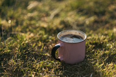 Gün batımında yeşil çimlerde kahve standı olan metal bir kupa.